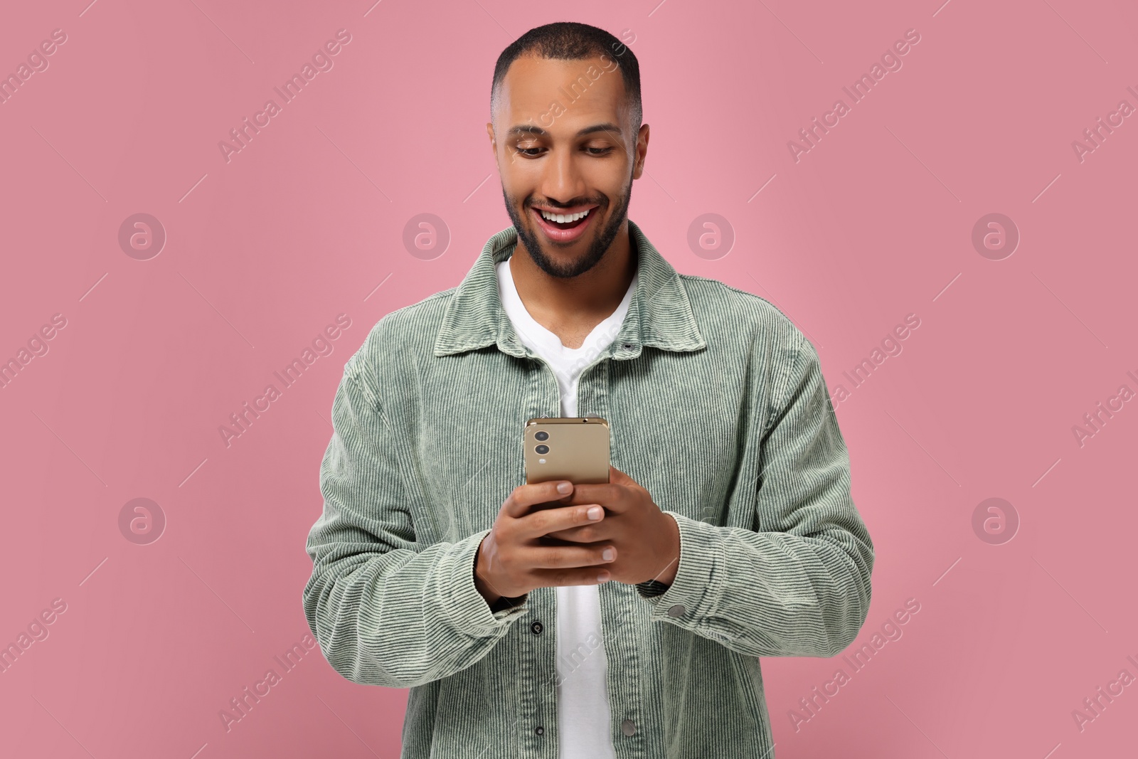 Photo of Happy man sending message via smartphone on pink background