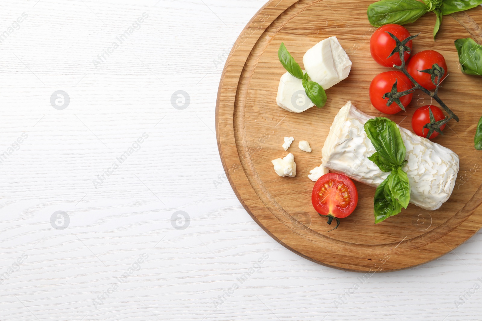 Photo of Delicious goat cheese with basil and tomatoes on white wooden table, top view. Space for text