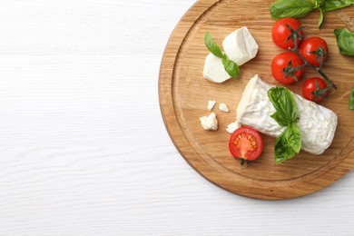 Photo of Delicious goat cheese with basil and tomatoes on white wooden table, top view. Space for text