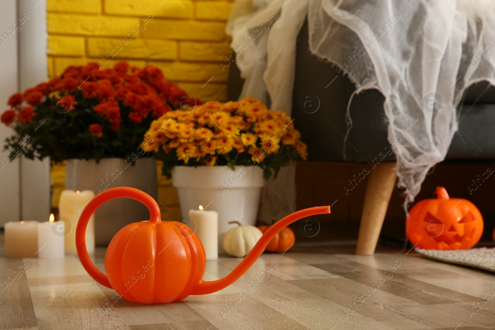 Photo of Pumpkin shaped watering can on floor in room, space for text. Halloween decor