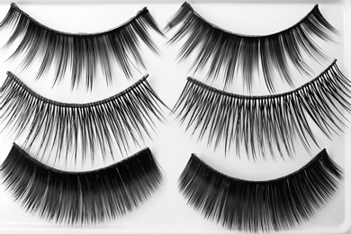 Different types of false eyelashes on light background, top view