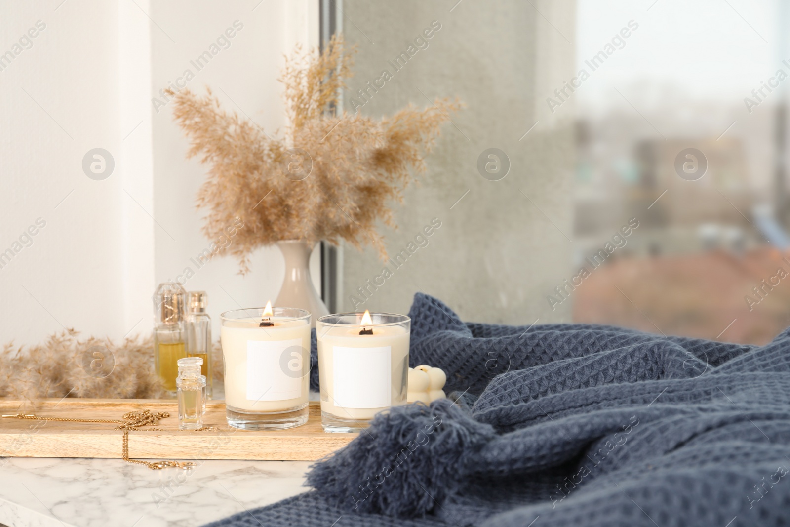 Photo of Burning soy candles, perfumes, blanket and stylish accessories on white window sill indoors
