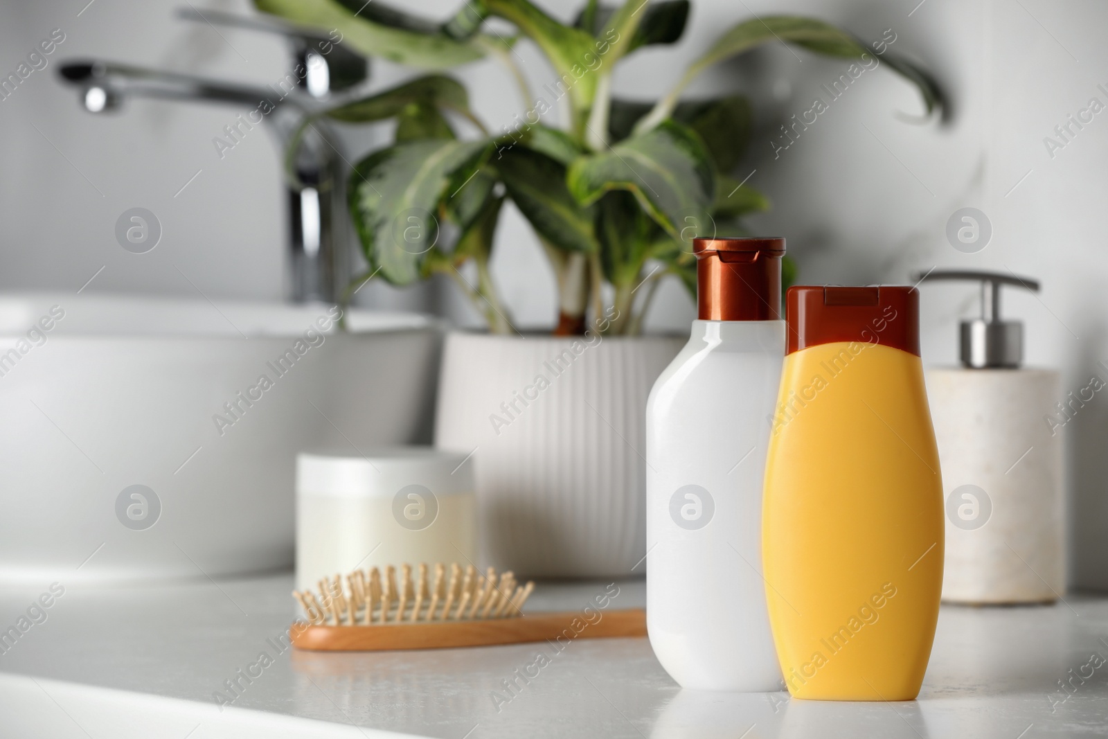 Photo of Shampoo, conditioner and wooden hairbrush near sink on bathroom counter, space for text