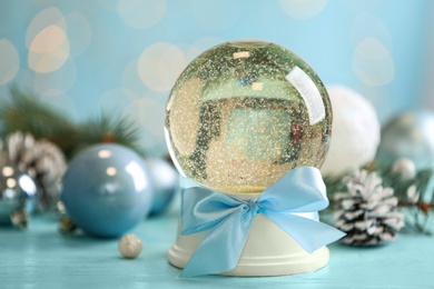 Photo of Beautiful snow globe and Christmas decor on light blue table, closeup