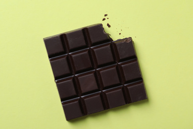 Tasty dark chocolate bar with bite mark on yellow background, top view