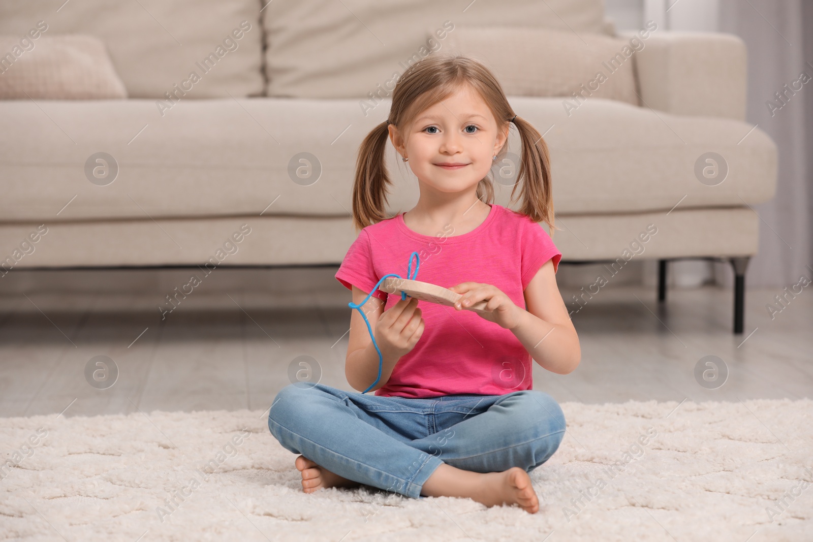 Photo of Cute little girl playing with wooden lacing toy indoors