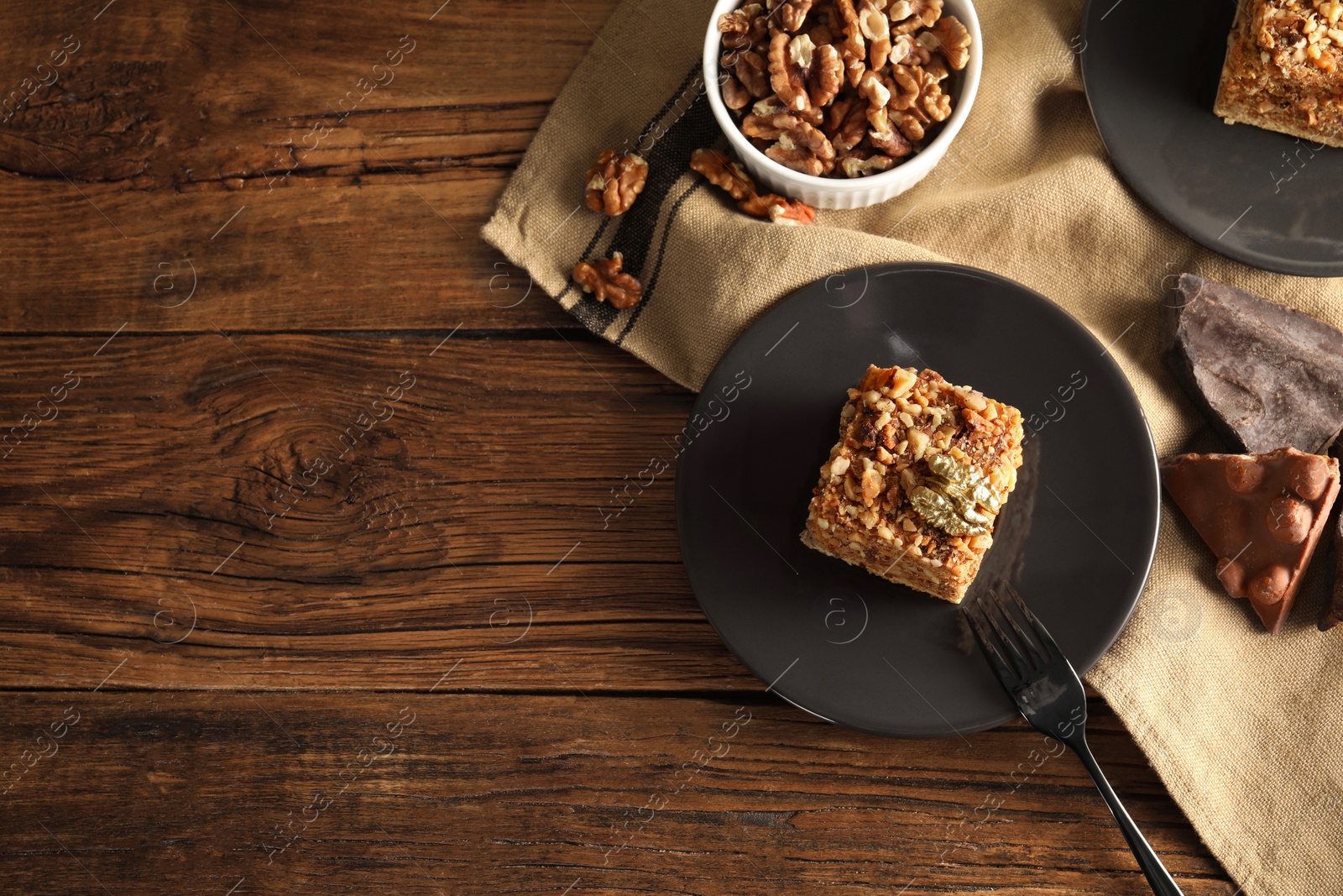 Photo of Pieces of honey cake, walnuts and fork on wooden table, flat lay with space for text
