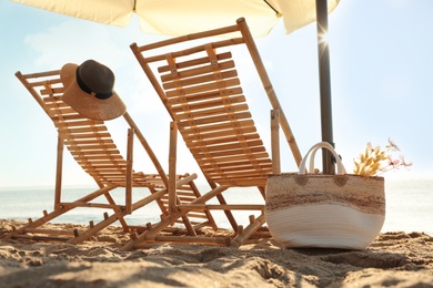 Wooden deck chairs, outdoor umbrella and bag with flowers near sea . Summer vacation