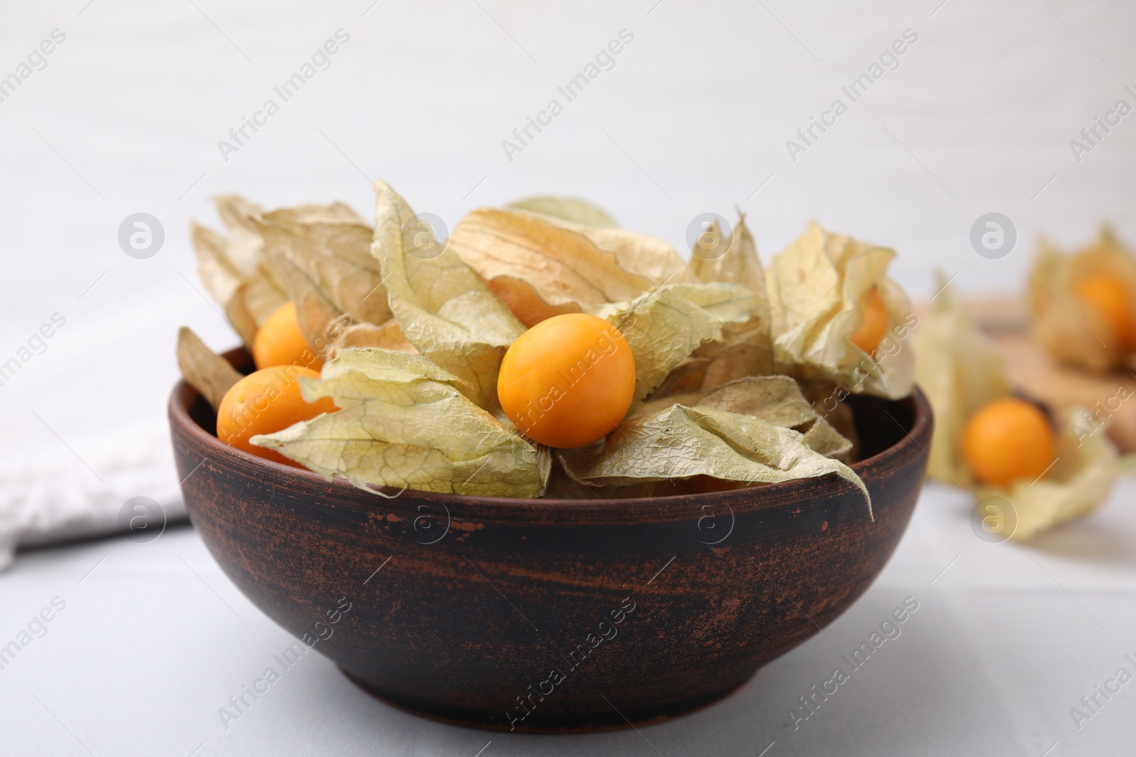 Photo of Ripe physalis fruits with calyxes in bowl on white table, closeup