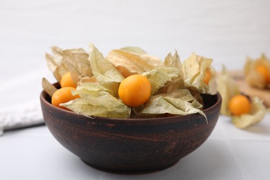 Ripe physalis fruits with calyxes in bowl on white table, closeup