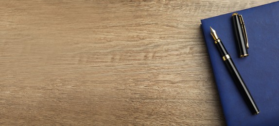 Image of Beautiful fountain pen and blue notebook on wooden table, top view with space for text. Banner design