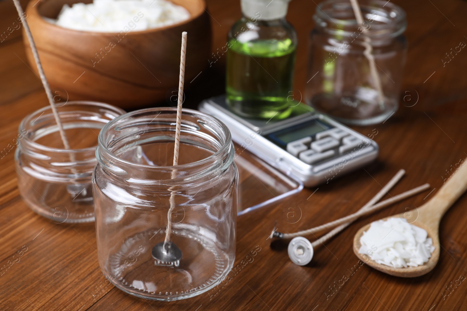 Photo of Glass jars with wicks and wax flakes on wooden table. Making homemade candles