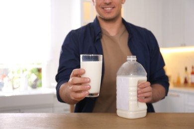 Man with glass and gallon bottle of milk at wooden table in kitchen, closeup