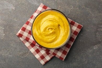 Photo of Tasty mustard sauce in bowl on grey textured table, top view