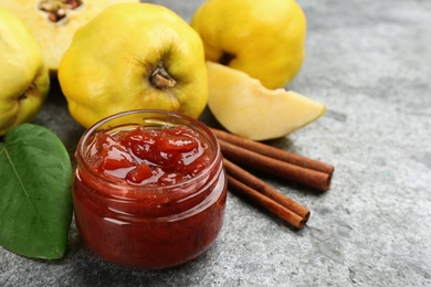 Photo of Delicious quince jam, fruits and cinnamon on grey table, closeup