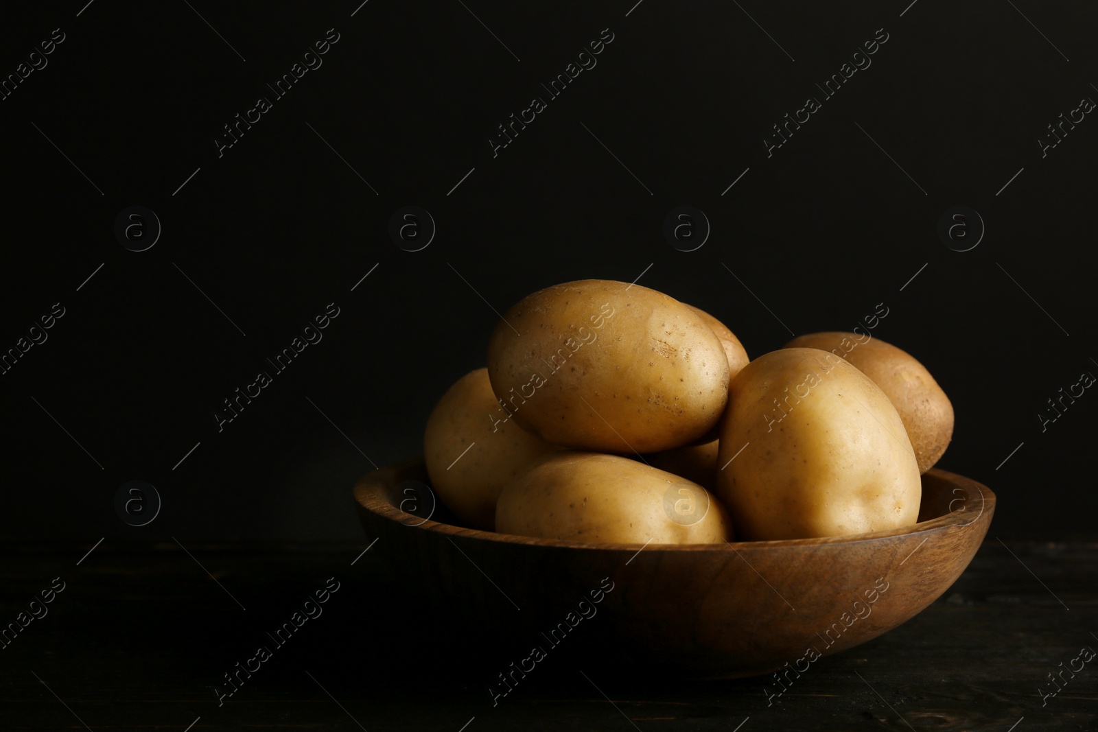 Photo of Fresh organic potatoes in bowl and space for text on black background