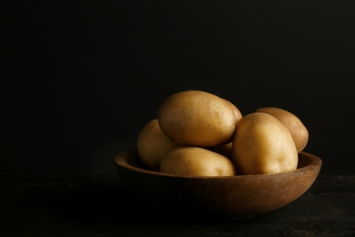 Fresh organic potatoes in bowl and space for text on black background