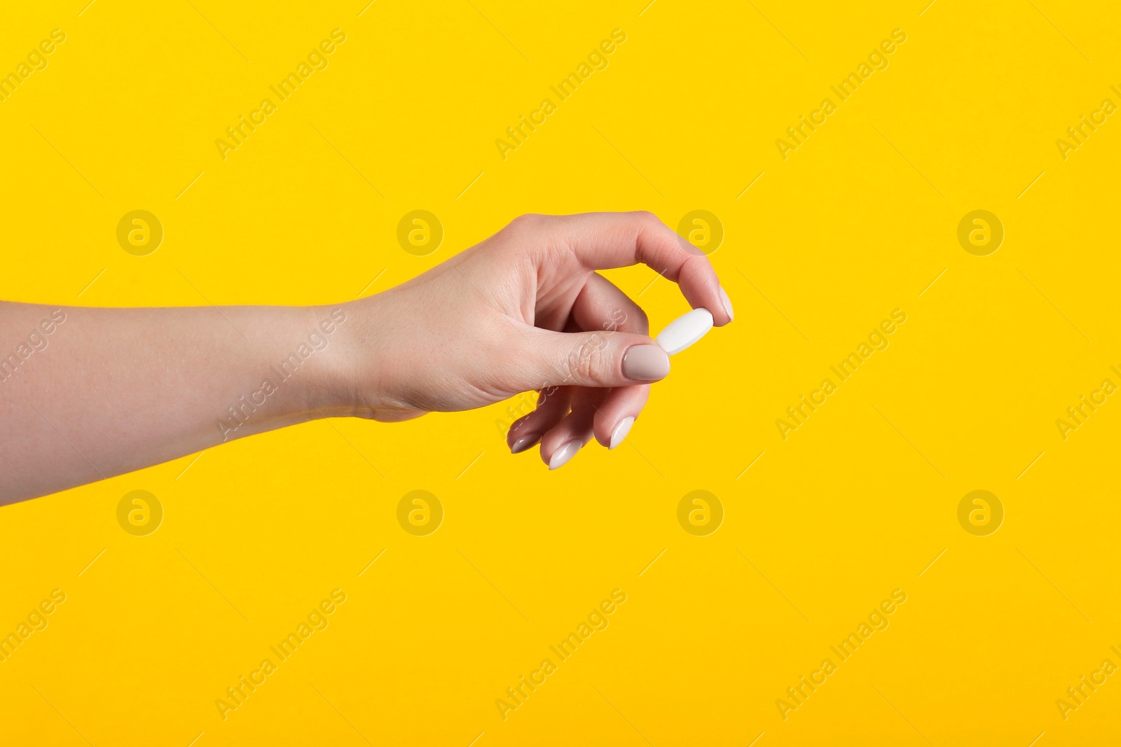 Photo of Woman holding vitamin pill on yellow background, closeup. Health supplement