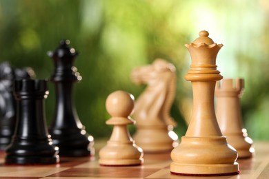 Photo of White wooden queen and other chess pieces on game board against blurred background, closeup