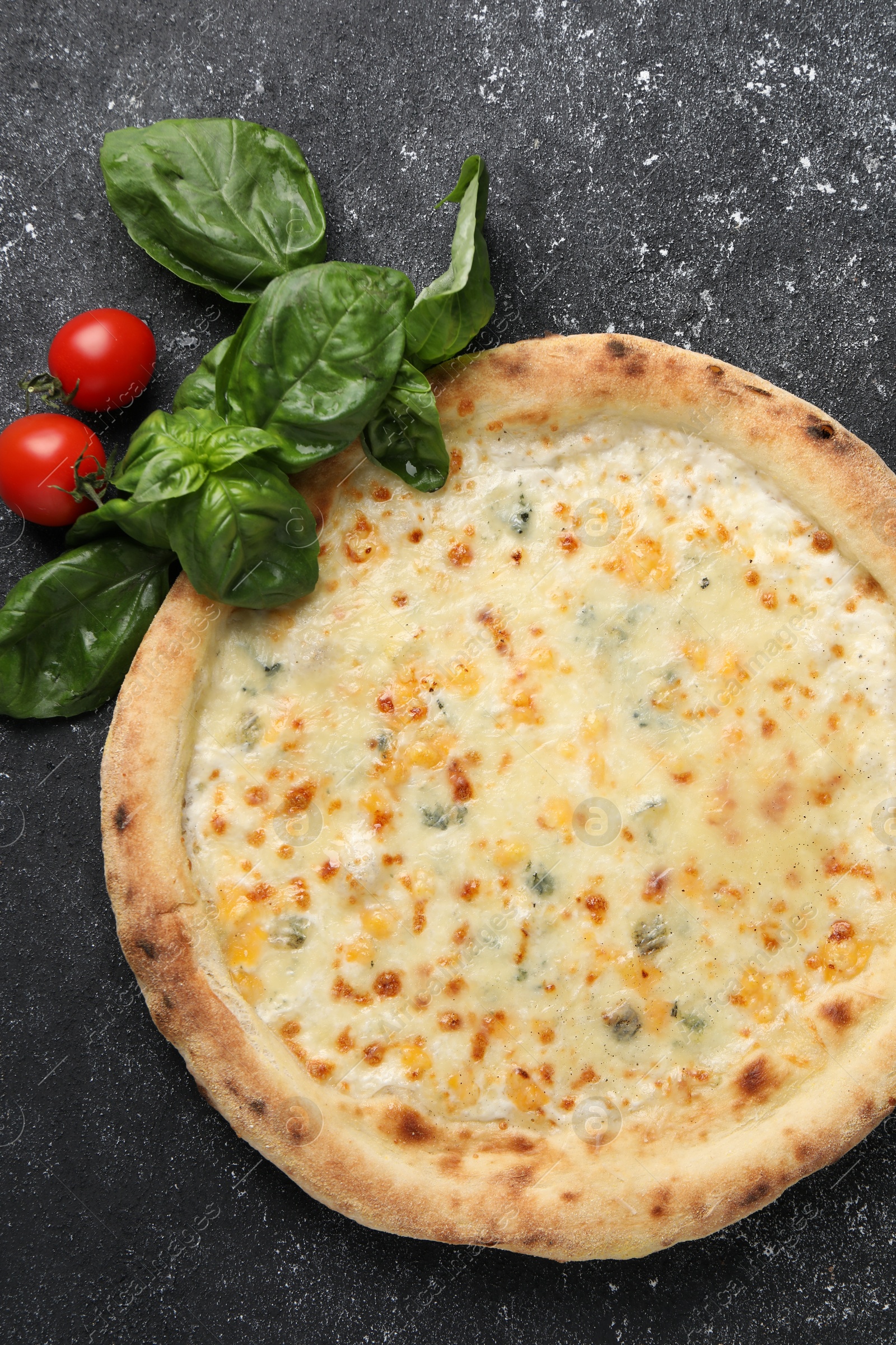 Photo of Delicious cheese pizza, basil and tomatoes on black textured table, flat lay