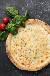 Photo of Delicious cheese pizza, basil and tomatoes on black textured table, flat lay