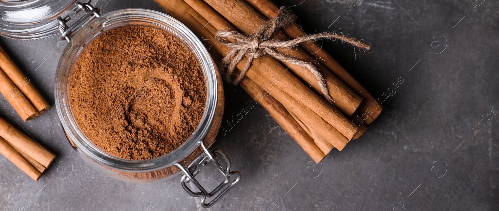 Photo of Aromatic cinnamon sticks and powder on grey table, flat lay. Space for text