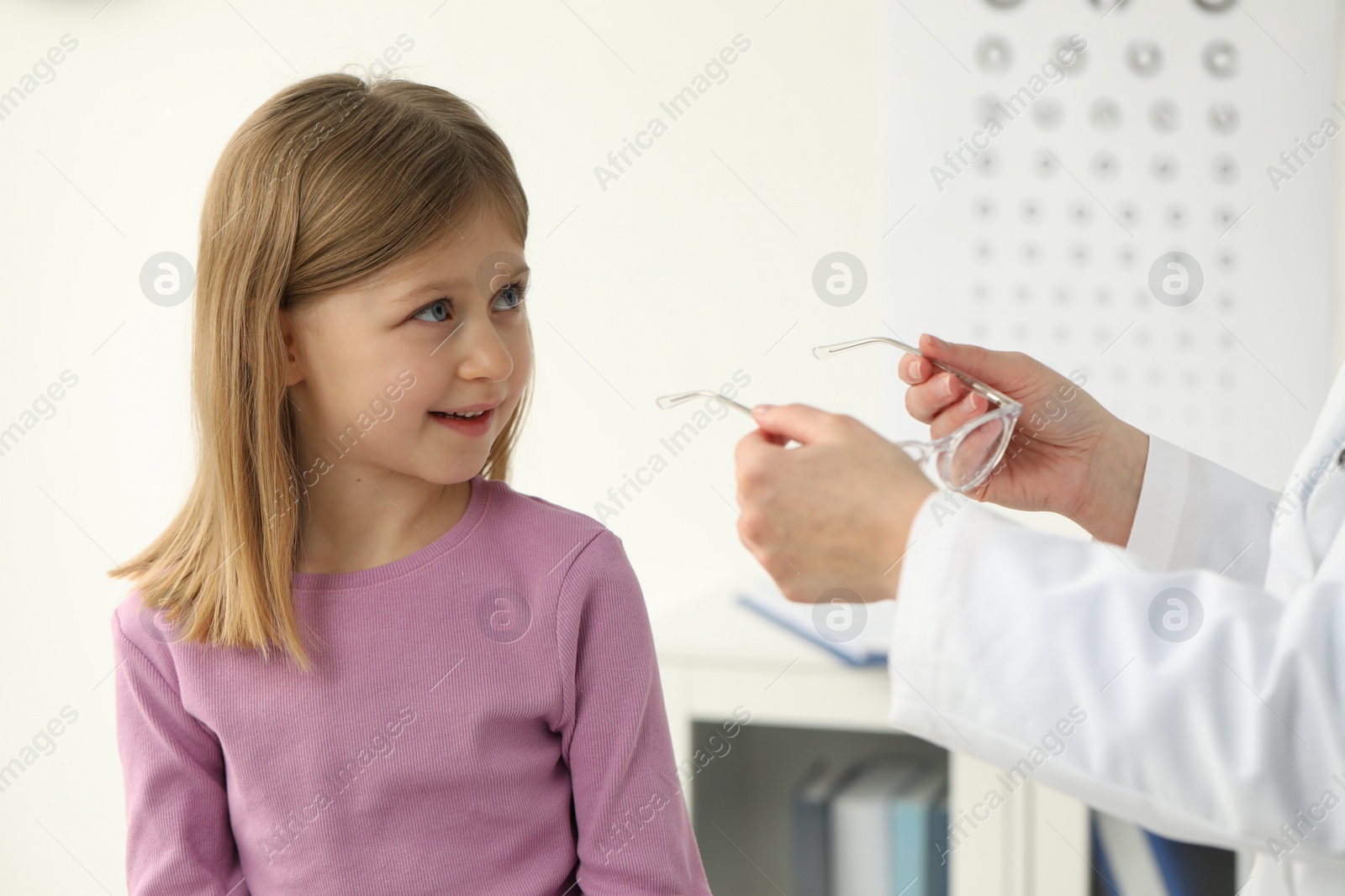 Photo of Vision testing. Ophthalmologist giving glasses to little girl indoors