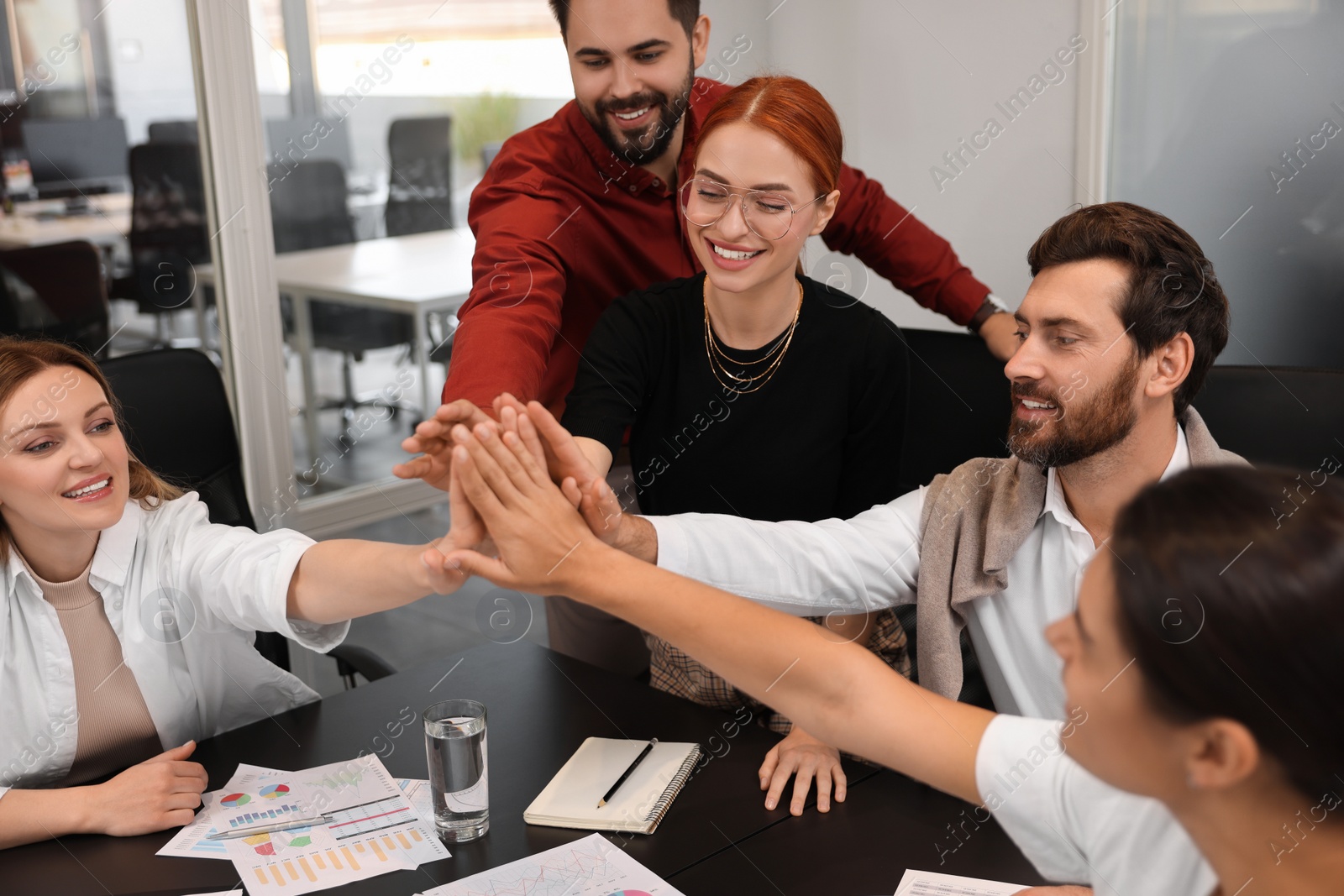 Photo of Team of employees joining hands in office