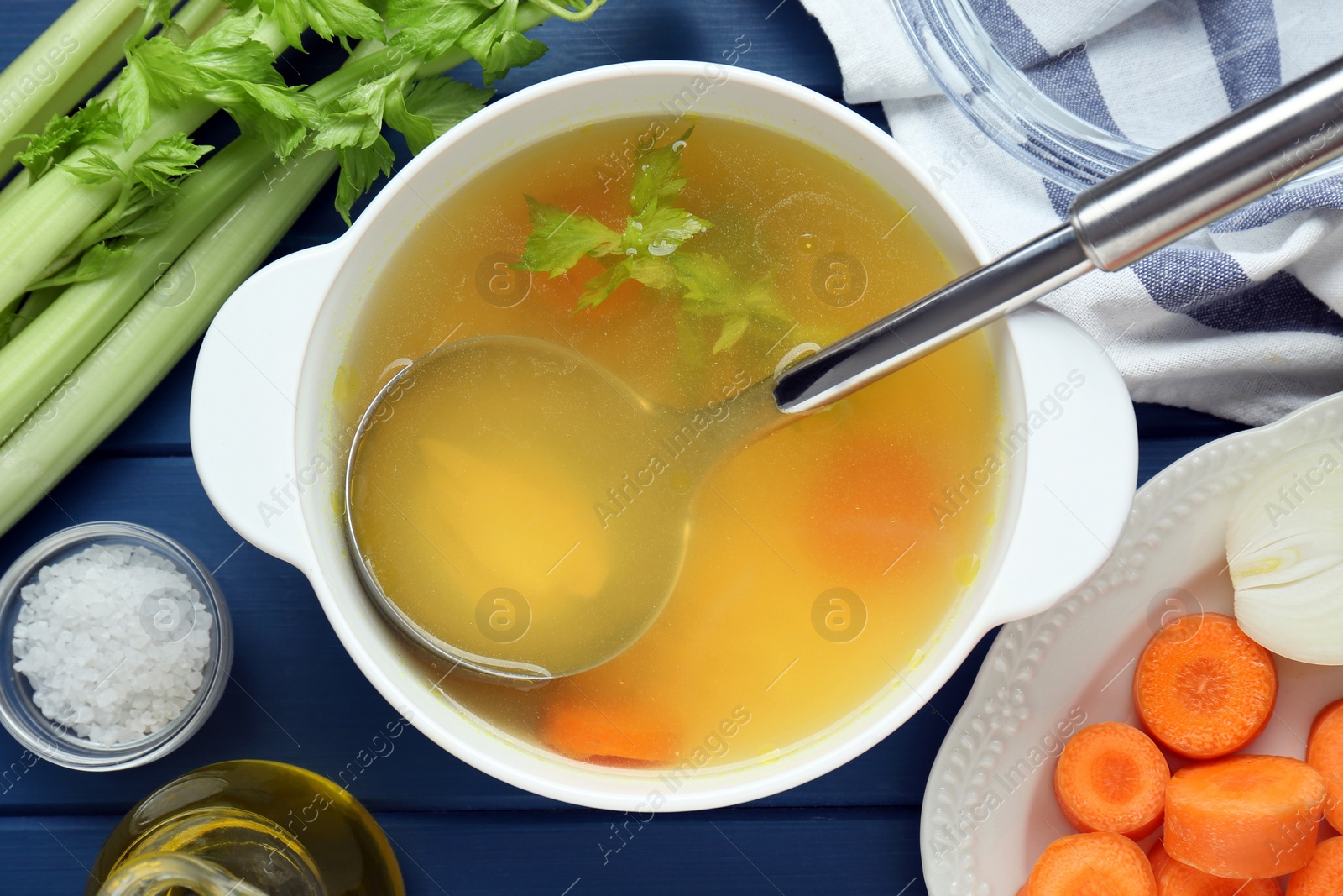 Photo of Delicious chicken bouillon and ingredients on blue wooden table, flat lay