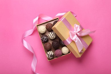 Photo of Open box with delicious chocolate candies and ribbon on pink background, top view