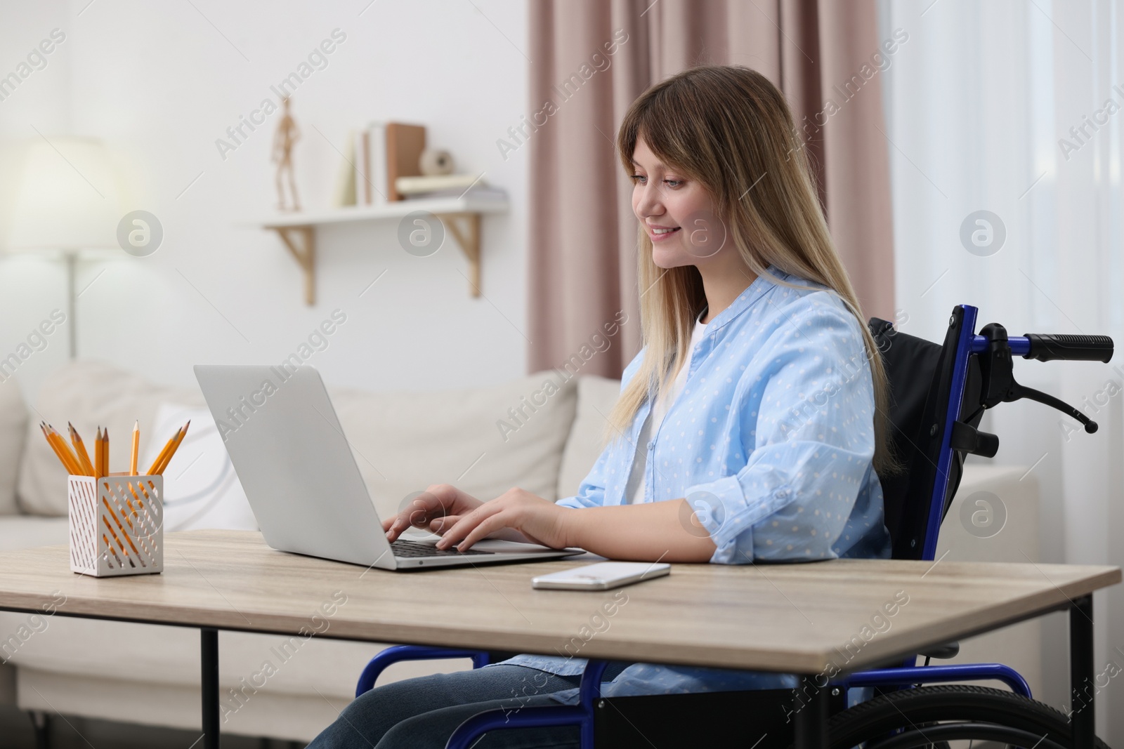 Photo of Woman in wheelchair using laptop at table in home office