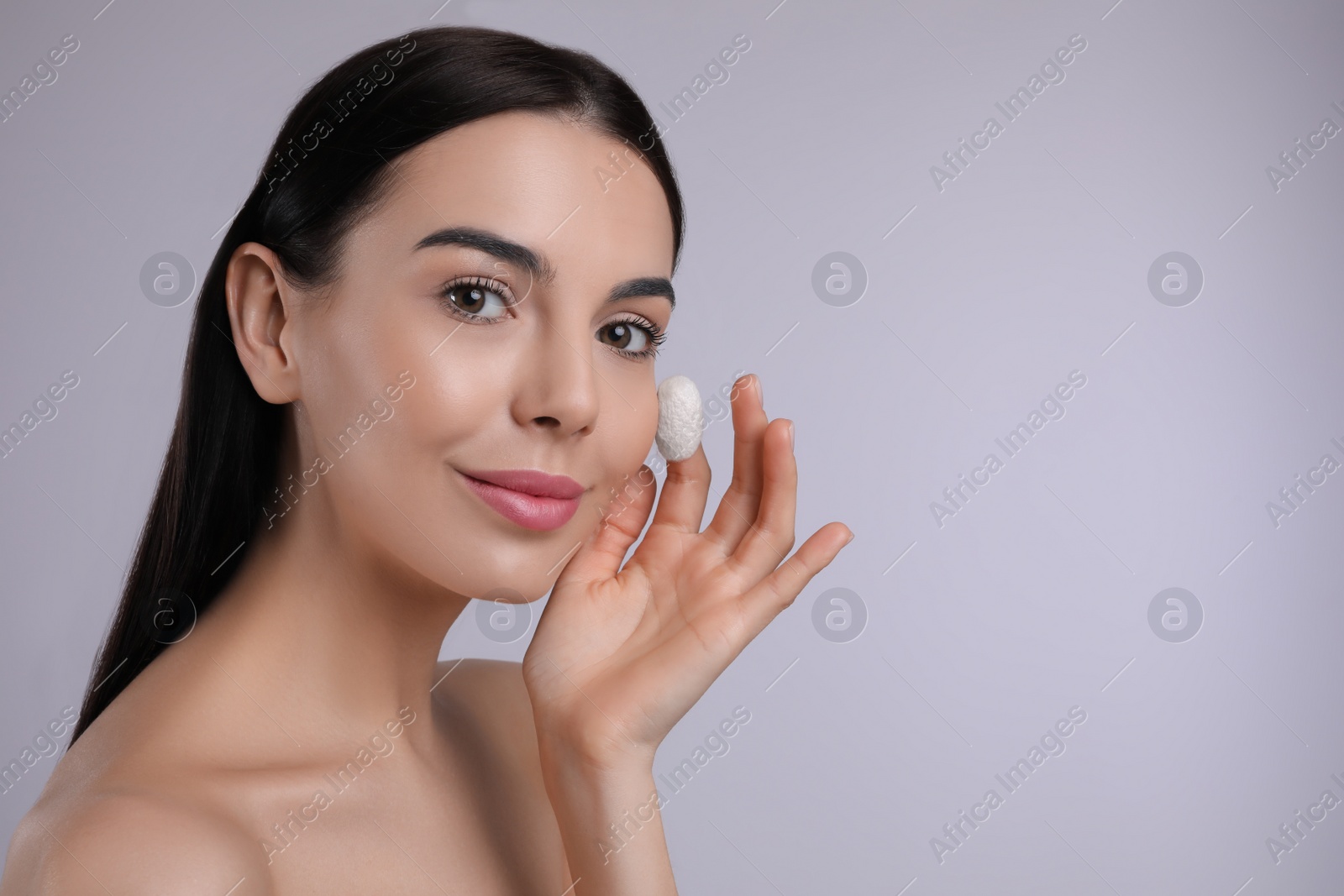 Photo of Woman using silkworm cocoon in skin care routine on light grey background. Space for text