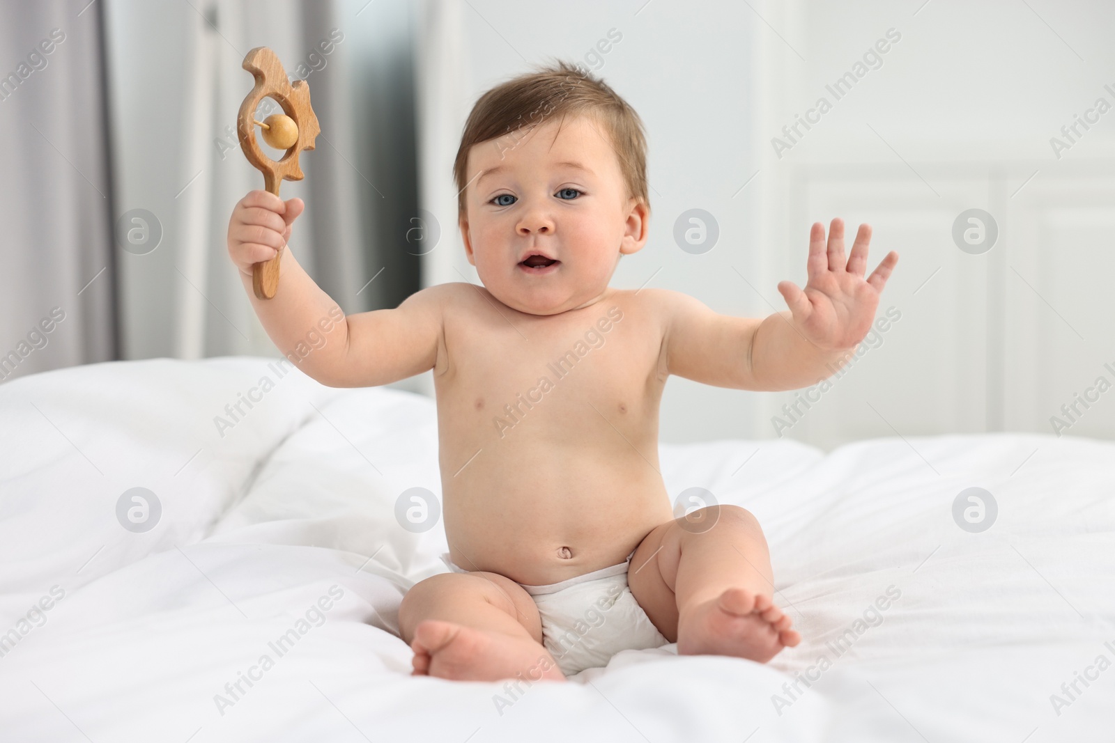 Photo of Cute baby boy with wooden rattle on bed at home