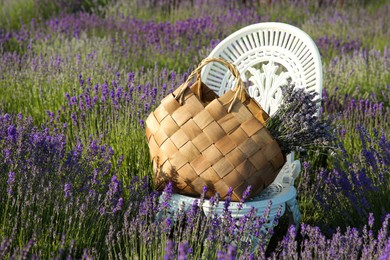 Wicker bag with beautiful lavender flowers on chair in field outdoors