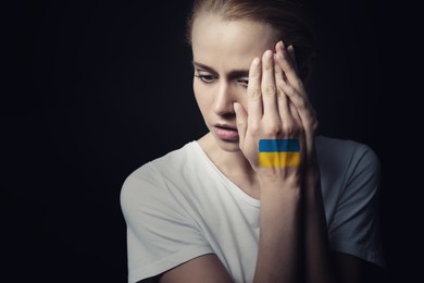 Image of Upset young woman with picture of Ukrainian flag on hand against black background. Stop war in Ukraine