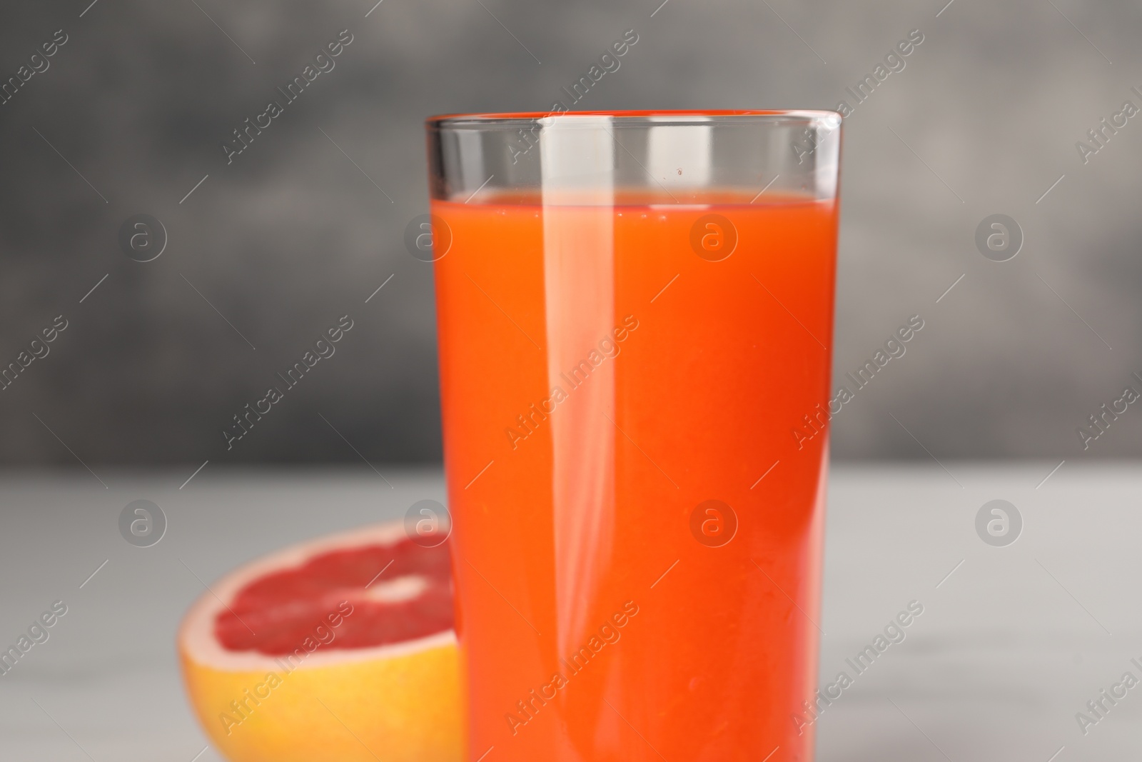 Photo of Tasty grapefruit juice in glass and fresh fruit on white table, closeup