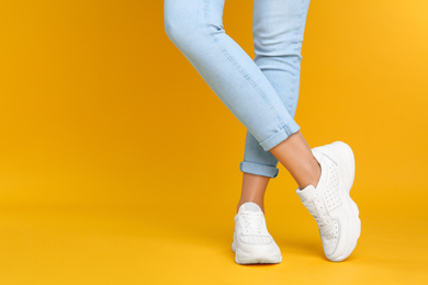 Woman wearing stylish sneakers on yellow background, closeup. Space for text