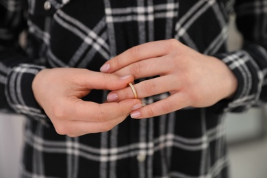 Photo of Woman taking off wedding ring indoors, closeup. Divorce concept