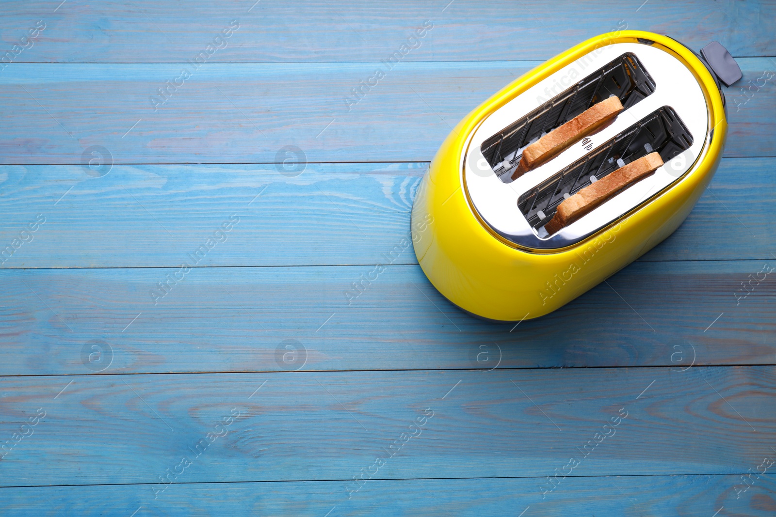 Photo of Yellow toaster with roasted bread on light blue wooden table, top view. Space for text