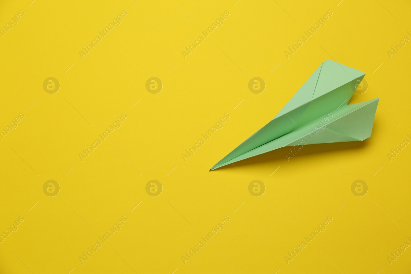 Photo of Handmade light green paper plane on yellow background, above view. Space for text