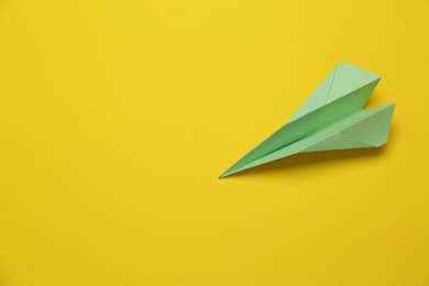 Handmade light green paper plane on yellow background, above view. Space for text