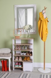 Wooden shelving unit with shoes and different accessories near green wall in hall. Storage idea