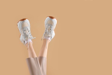 Woman wearing pair of new stylish sneakers on beige background, closeup. Space for text