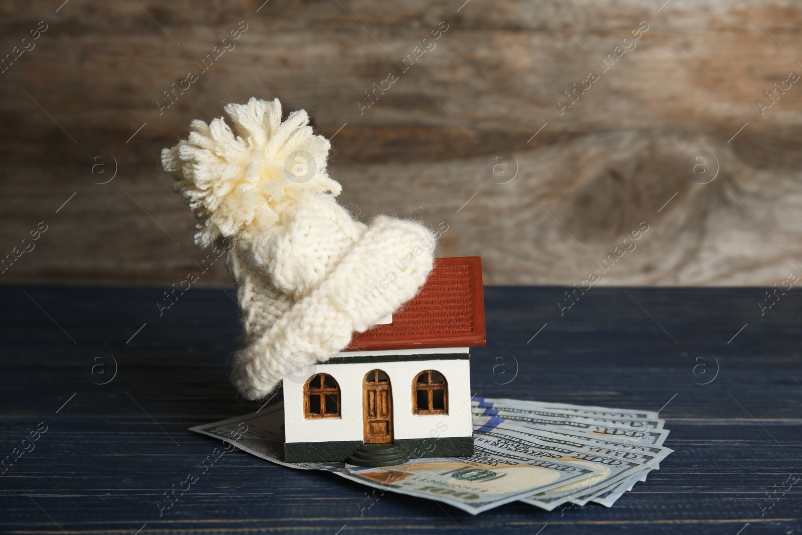 Photo of House model with warm hat and money on table against wooden background. Heating expenses