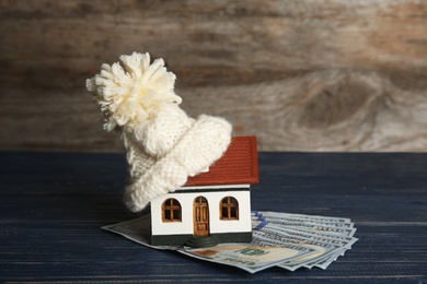 Photo of House model with warm hat and money on table against wooden background. Heating expenses