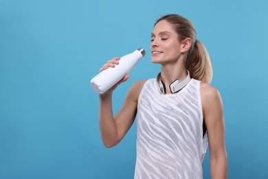 Photo of Sportswoman with thermo bottle and headphones on light blue background, space for text