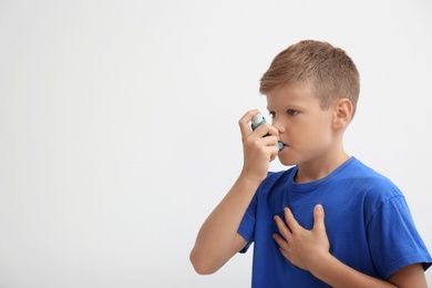 Photo of Little boy using asthma inhaler on light background