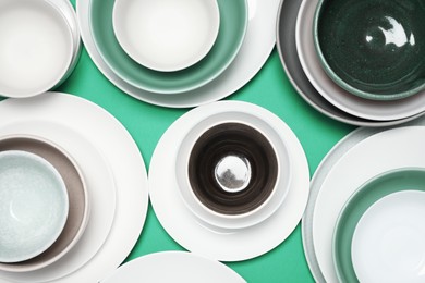 Photo of Different plates and bowls on green background, flat lay