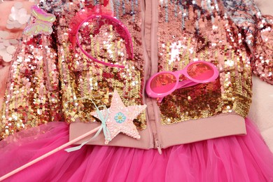 Stylish carnival costume with sequins, sunglasses, headband and wand on pink fabric, above view