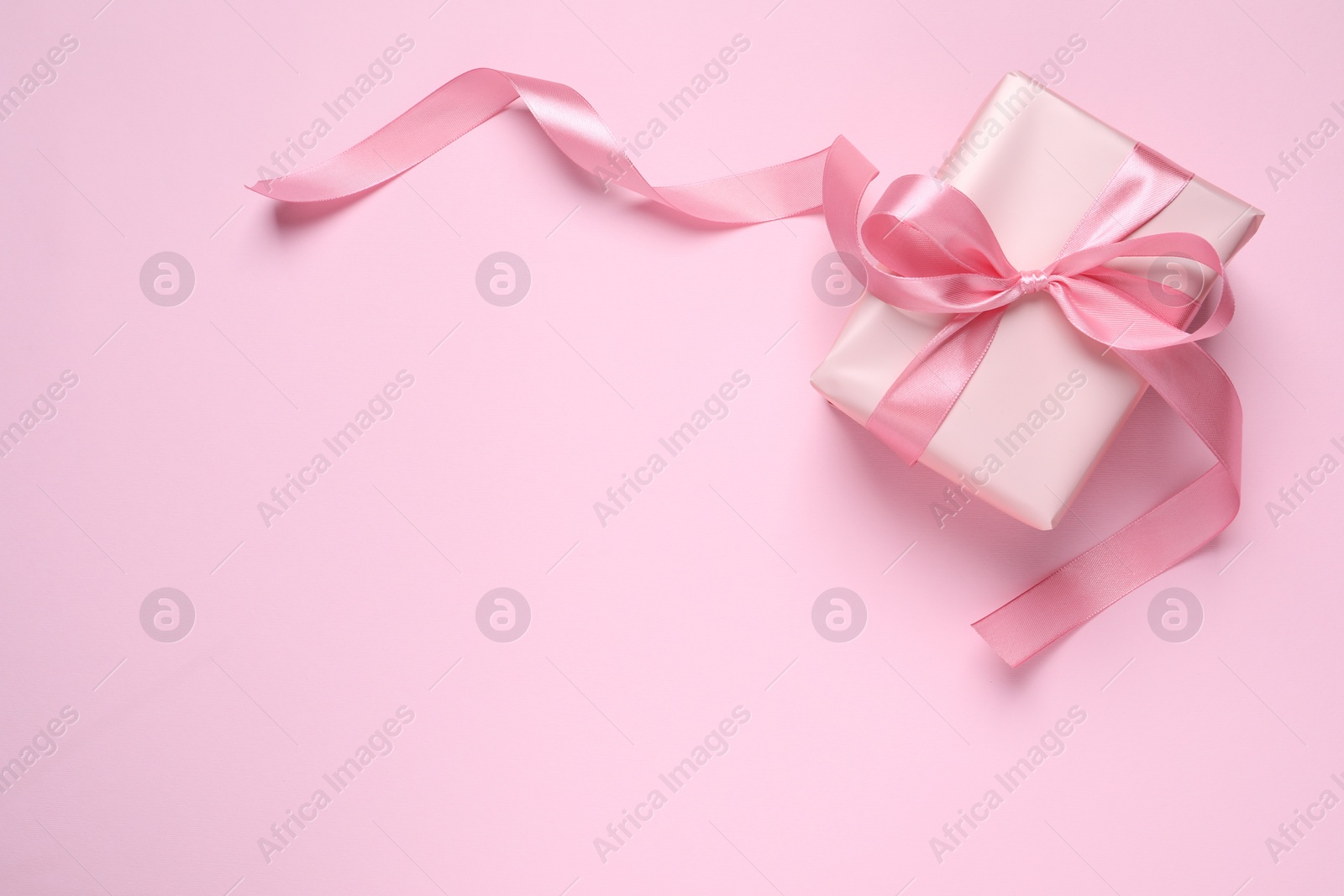 Photo of Beautiful gift box with bow on pink background, top view. Space for text